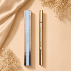 Marom ROSE BERRY dual ended dark brown eyebrow pencil and spoolie brush in gold packaging on a beige fabric background