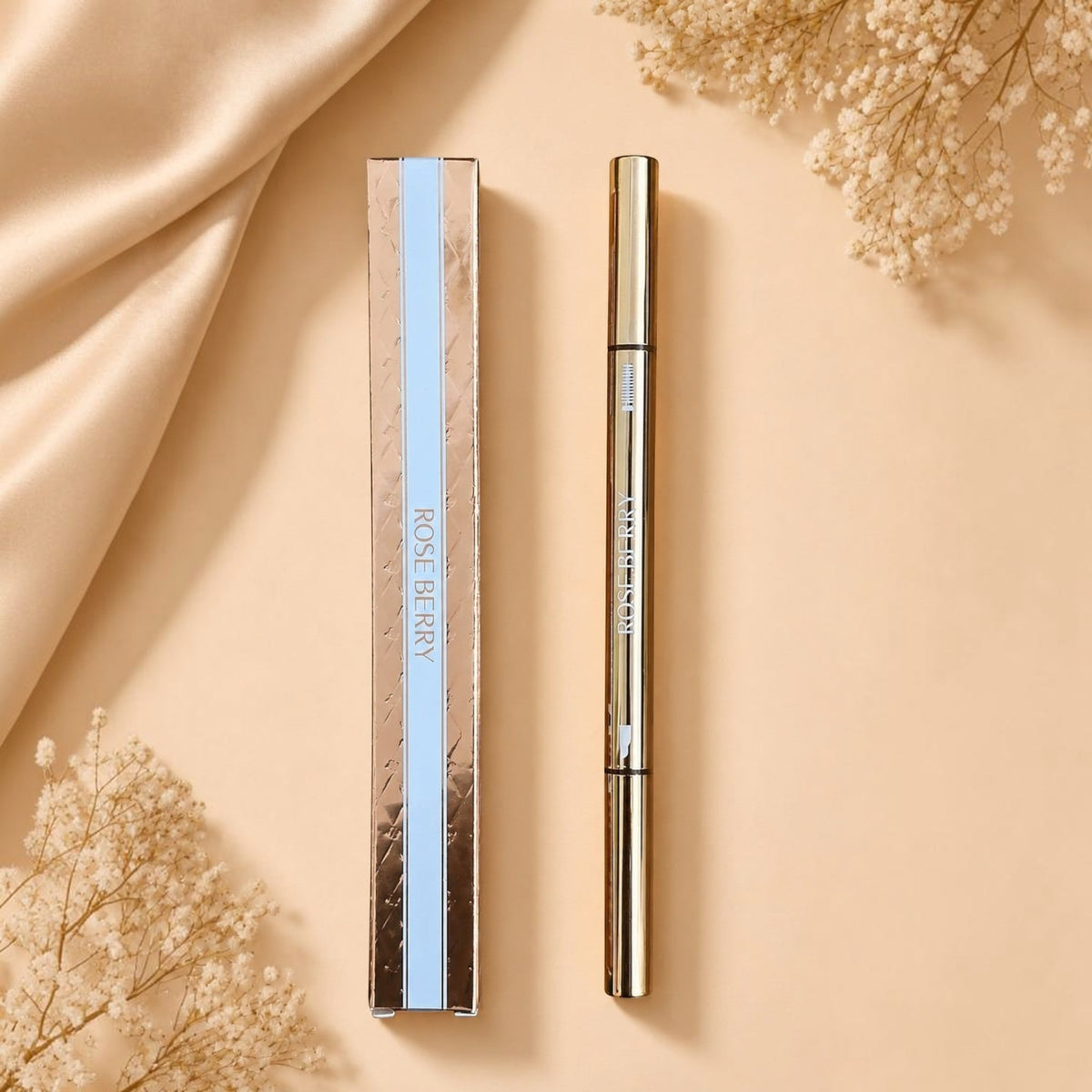 Marom ROSE BERRY dual ended dark brown eyebrow pencil and spoolie brush in gold packaging on a beige fabric background