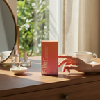 Marom Rose Berry Filler Comfy Smooth SPF 50 sunscreen box on a wooden vanity table with a hand reaching towards it